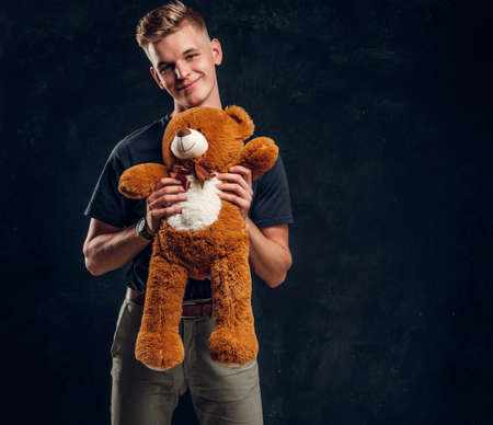 Pretty happy teenager posing with big plush bear over grey background at dark photostudio.の写真素材
