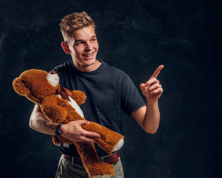 Young attractive man is showing something exiting for his friend giand toy bear at dark studio.の写真素材