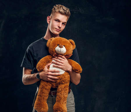 Pretty happy teenager posing with big plush bear over grey background at dark photostudio.の写真素材