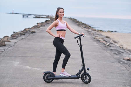 Atractive happy woman is enjoying morning riding with her new electrical scooter at seaside.の写真素材