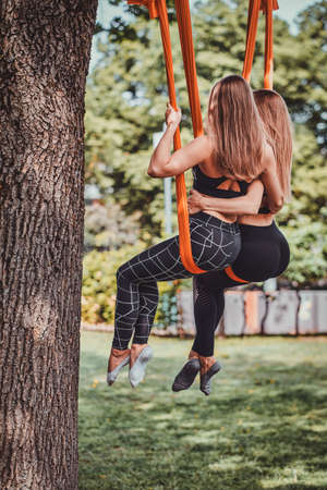 Couple of best friends are chilling on the orange slings under the tree in the summer park.の写真素材