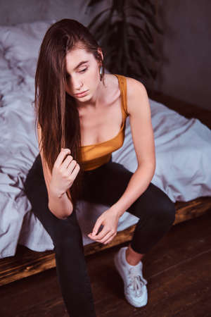 Pretty sexy woman is sitting on the bed in her bedding room. She has long hair.