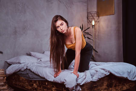 Pretty sexy woman is sitting on the bed in her bedding room. She has long hair.