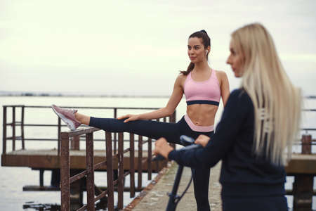 Two beautiful girls have gymnastic at seaside. One of them has electro scooter, another is doing...