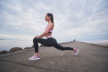 Attractive sportive women in activewear is doing lunge off exercise at seashore.の写真素材