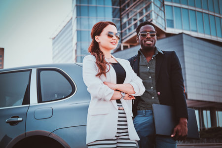 Attractive sucessful business partners in sunglasses are meeteng up near big offices building.