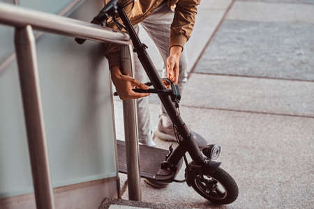 Young casual man is locking his electrical scooter near his job at street.の写真素材