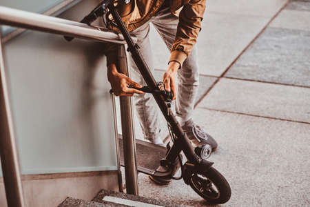 Young casual man is locking his electrical scooter near his job at street.の写真素材
