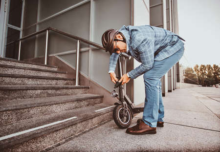 Modern trendy man is locking his electrical scooter near his job at street.の写真素材