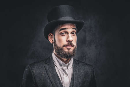 Portrait of a stylish bearded male in an elegant suit and cylinder hat, looking at a camera over dark background.の写真素材