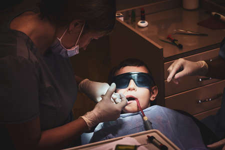 Brave small child gets a dental treatment by expirienced doctor at dental clinic.の写真素材