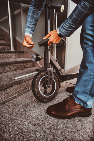 Modern trendy man is locking his electrical scooter near his job at street.