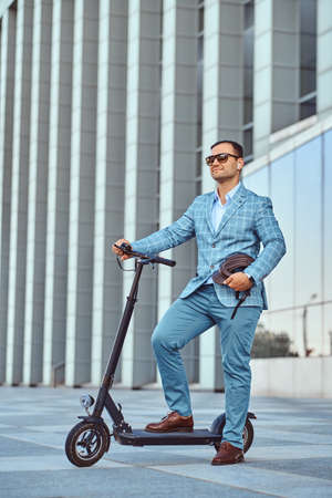 Cheerful modern man is driving his electro scooter near his office after long hard day.の写真素材