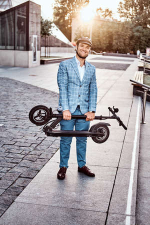 Happy smiling man is holding his new electro scooter in folded position while going to his office.の写真素材