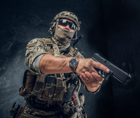 Serious brave soldier in military uniform and sunglasses is aiming with his gun.