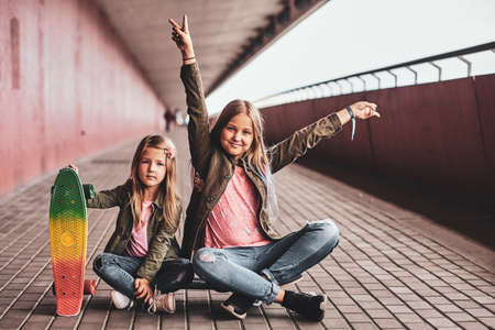 Two little cheerful sisters are sitting on the skateboard in the tunnel.の写真素材