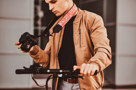 Young pensive photographer with scooter is watching photos on his digital photo camera.