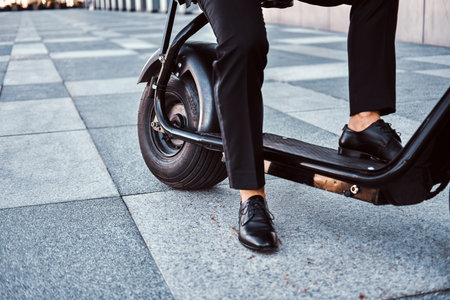 Elegant businessman in black suit is sitting on his electrical scooter near his office.
