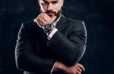 Sceptical bearded man in suit and white shirt is posing for photographer at dark studio.の写真素材