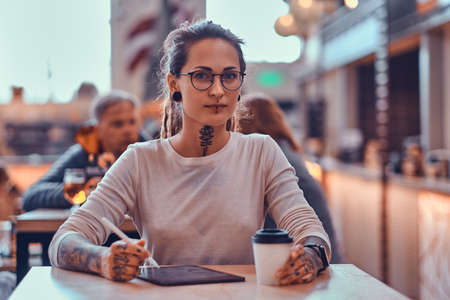 Young pretty woman with tattooes on her hands is enjoying her time at food court with her sketching pad.の写真素材