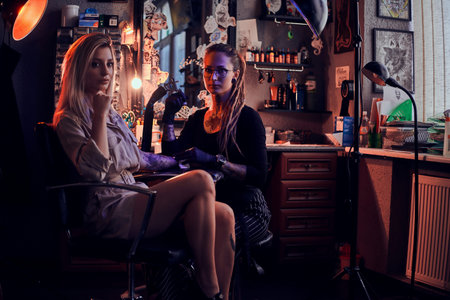 Creative tattoo master with dreadlocks is creating beautiful tattoo on womans hand at tattoo salon.の写真素材