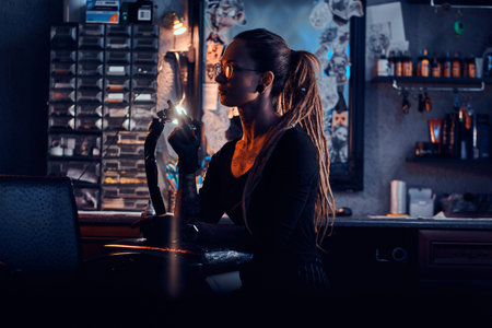 Portrait of young woman with dreadloks and glasses which is sitting at her tattoo studio.