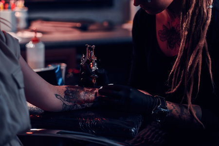Closeup photo shoot of tattoo making, artist is working with tattoo machine on customers hand.