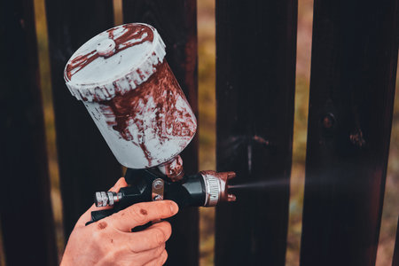 Closeup photo shoot of fences renovation. Man is applying paint with airbrush.
