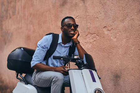 Smiling cheerful student on the scooter is waiting for his friend at quaet street.の写真素材