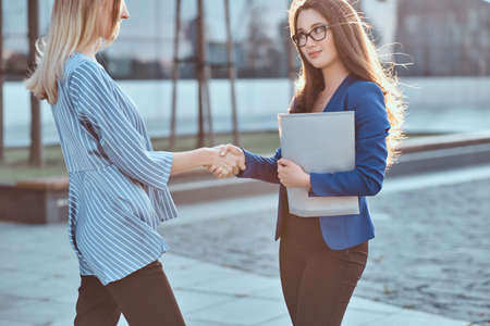 Couple of serious businesswomen have unformal meeting outside, they are greeting one each other with handshake.の写真素材