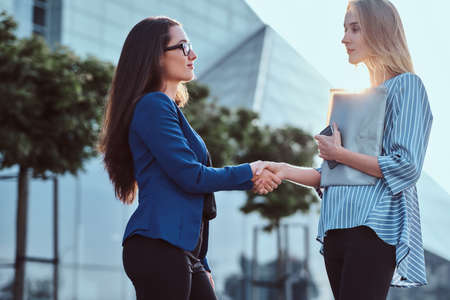 Couple of serious businesswomen greeting one each other with handshake outside of their offices.の写真素材