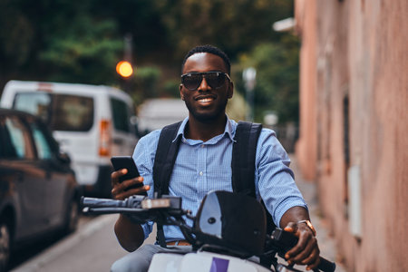 Smiling cheerful student on the scooter is waiting for his friend at quaet street.