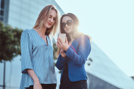 Two attractive friends are watching something interesting on mobile phone on the street.