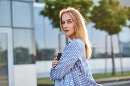 Young successful businesswoman is waiting her new partner on the street with mobile phone in her hands.の写真素材