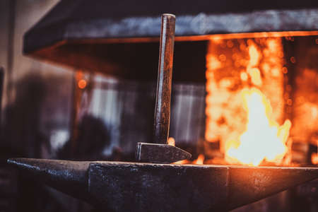 Hammer on anvil at dark blacksmith workshop with fire in stove at background.の写真素材