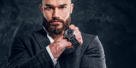 Successful serious man is posing for photographer with watch on his fist on the dark background.の写真素材