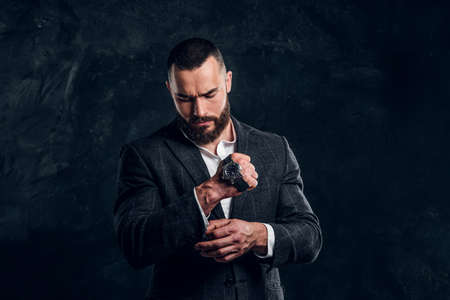 Successful serious man is posing for photographer with watch on his fist on the dark background.の写真素材