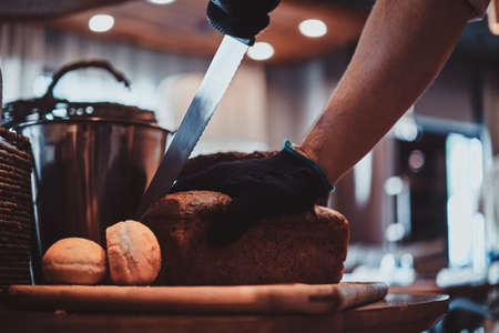 Expirienced baker in protective gloves is slicing bread for daily breakfast at restaurant.の写真素材