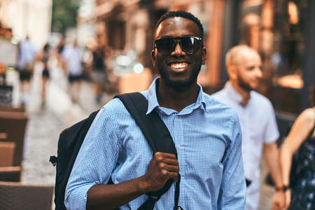 Cheerful smiling american tourist is walking on the street with his backpack.の写真素材