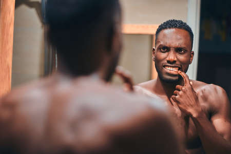 Handsome african man is checking his teeth in the bathroom while see himself in the mirror.の写真素材