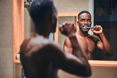 Attractive young man is brushing his teeth in the bathroom while see himself in the mirror.の写真素材