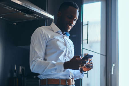 Happy smiling businessman is enjoying his morning coffee while chatting by mobile phone at his kitchen.の写真素材