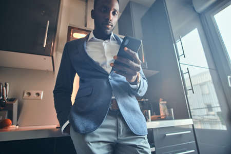 Young african man in white shirt is chatting by mobile phone at the kitchen.の写真素材