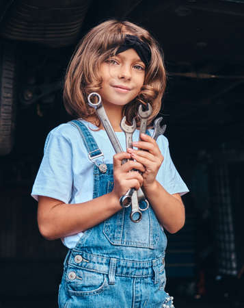 Pretty cheerful girl is holding wrenches in hangs while posing for photographer at auto service.の写真素材