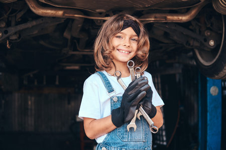 Pretty cheerful girl is holding wrenches in hangs while posing for photographer at auto service.