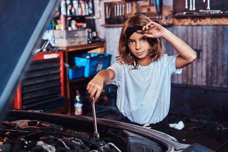 Little pretty girls is dreaming to be at auto technicial, she is trying to fix broken car.の写真素材