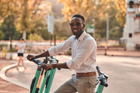 Cheerful smiling man is choosing right scooter from parking at bright sunny day.の写真素材