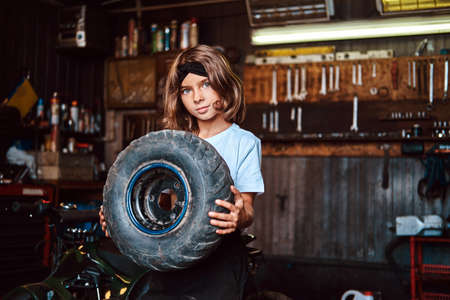 Nice small girl is posing for photographer with big wheel from car at auto service.の写真素材