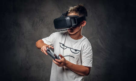 Little trendy kid is playing new videogame using special virtual reality goggles and joystick.の写真素材