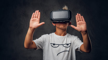 Young pretty schoolboy is playing virtual video game wearing special goggles.